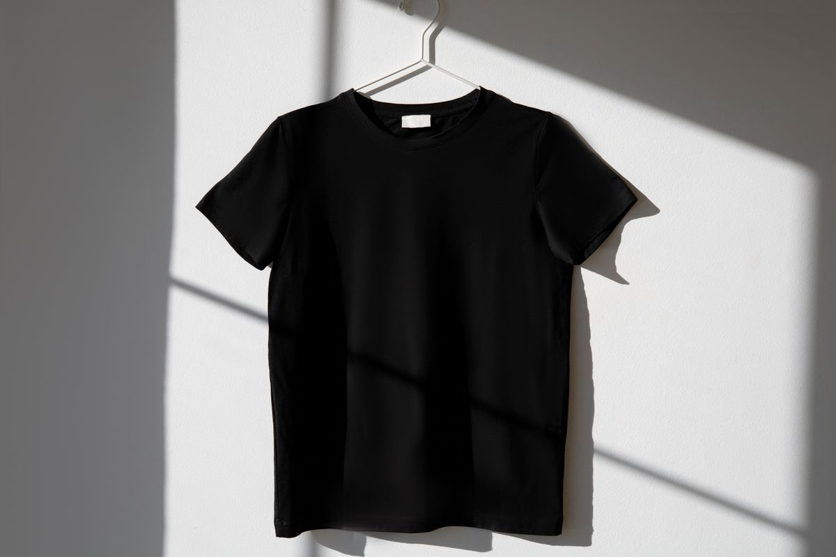 Blank black T-shirt mockup hanging against a light studio wall